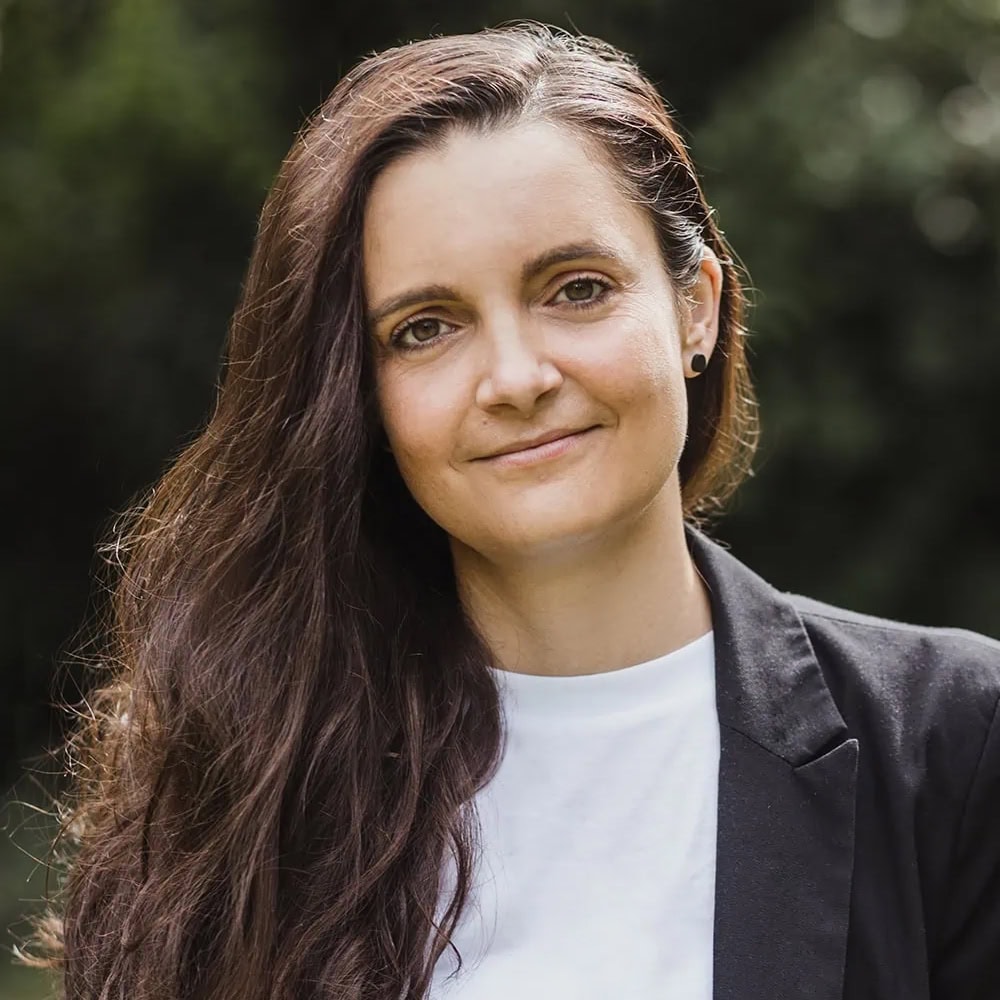 Porträt von Online-Pfarrerin Jennifer Scherf. Sie lächelt in die Kamera und trägt einen schwarzen Thala. Im Hintergrund ist eine verschwommene, helle Umgebung zu sehen.